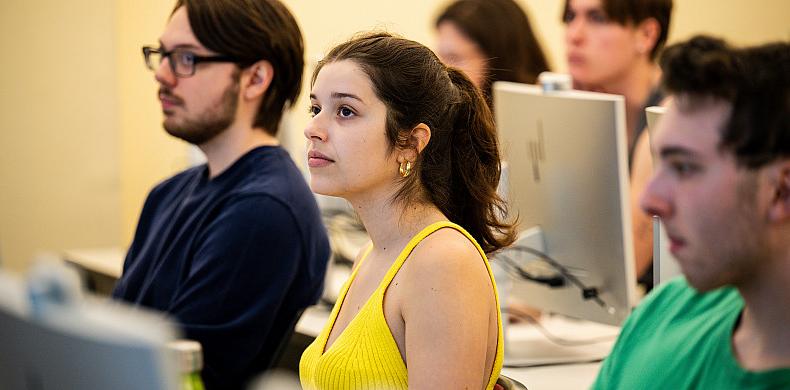 Students sit in front of computers in a classroom.